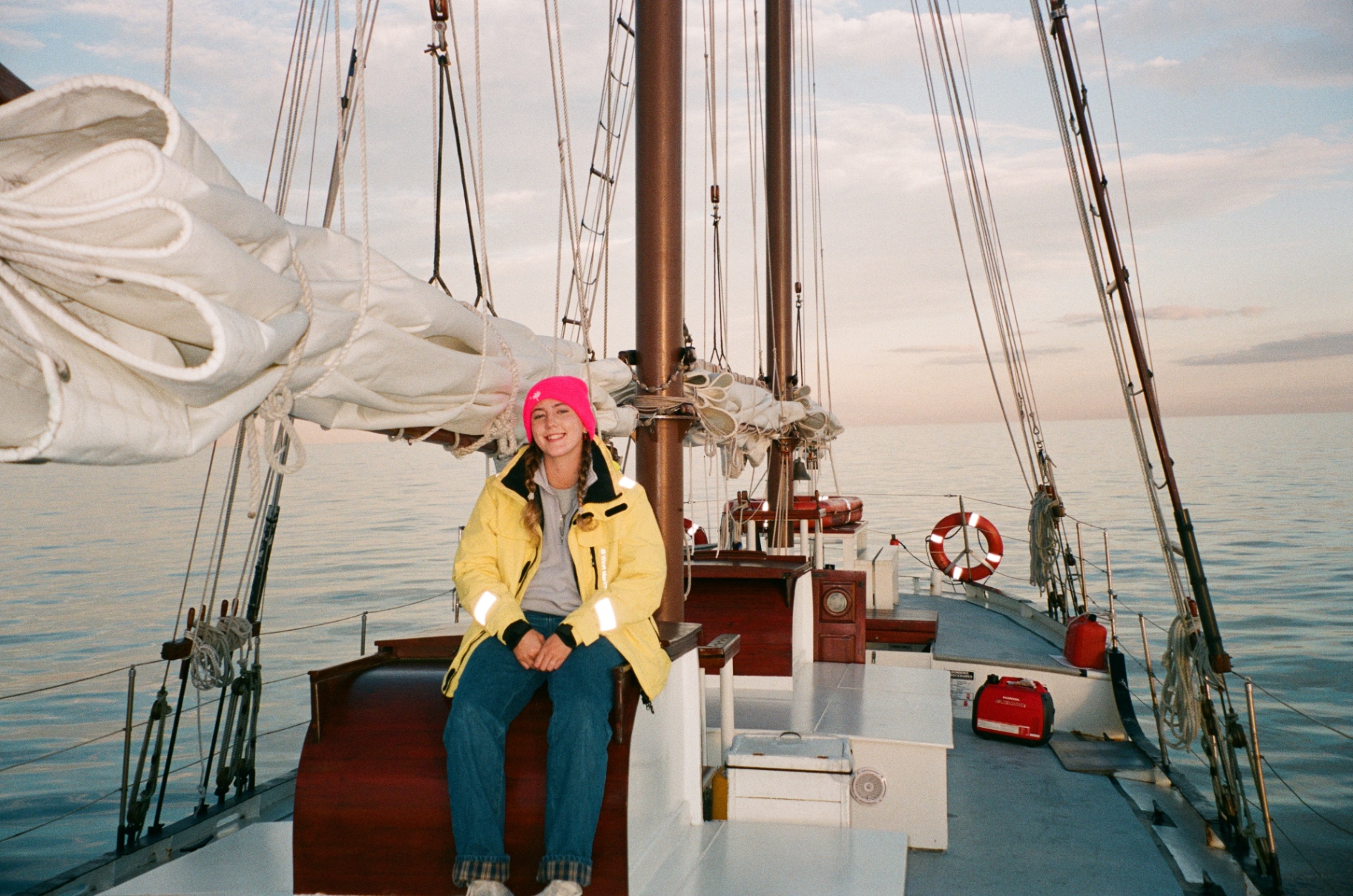 A Maritime Gal in a bright yellow jacket sitting on a classic sailboat at calm seas