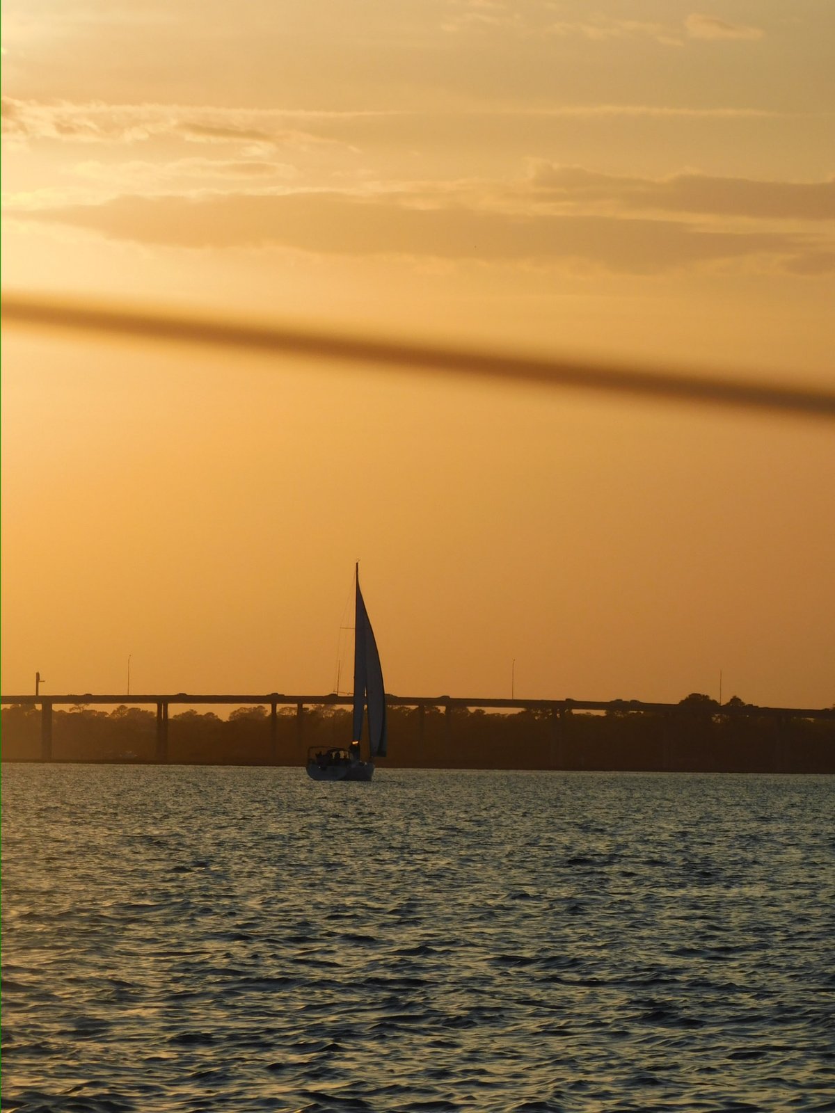 A sailboat silhouetted against a golden Charleston sunset