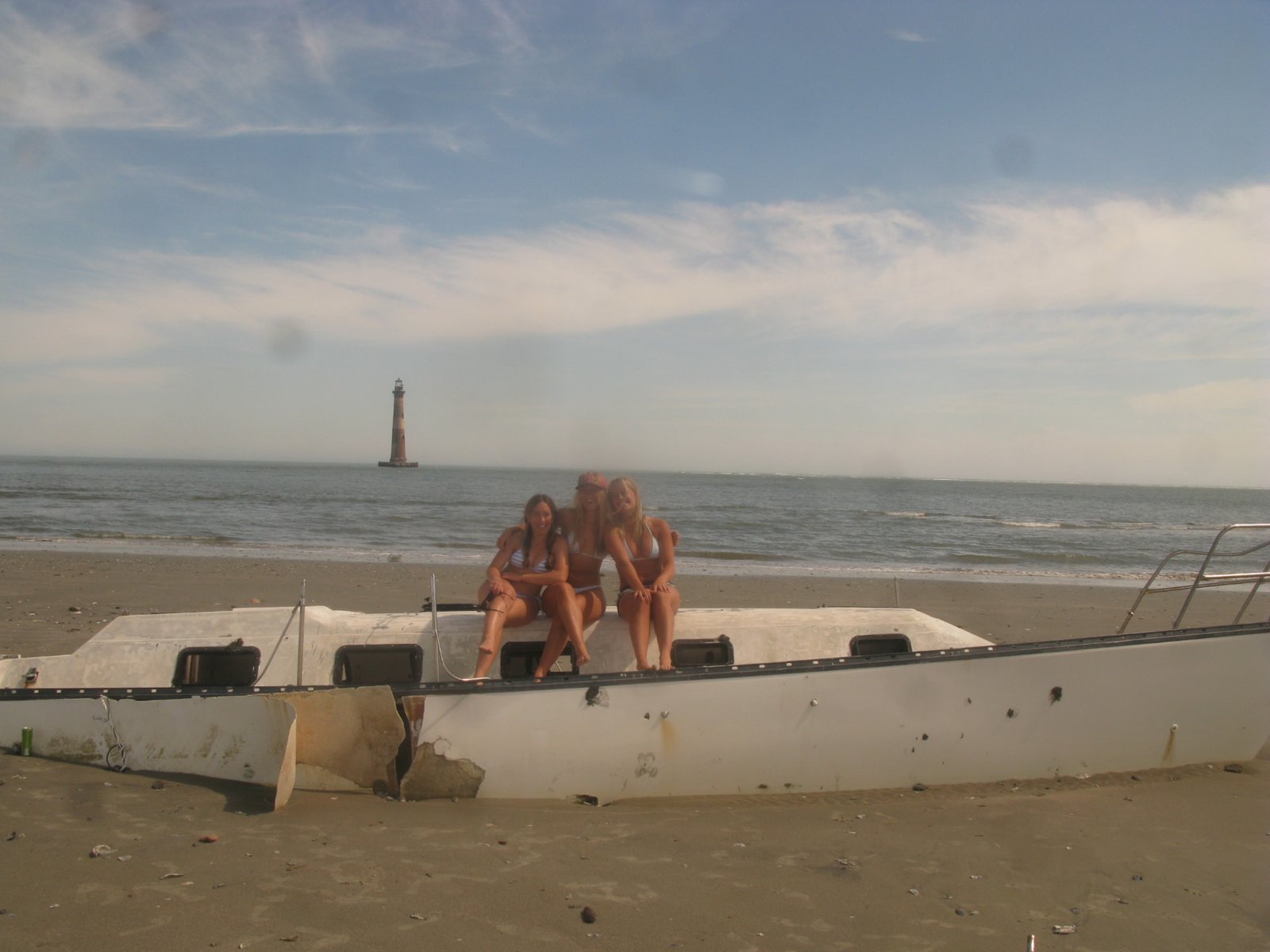 Three gals sitting on a beached hull near Morris Island Lighthouse
